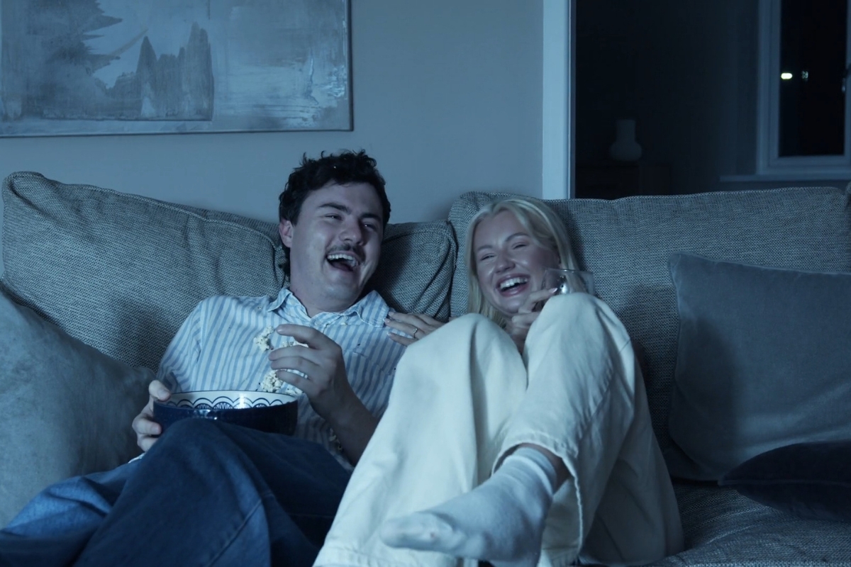 momak i devojka se smeju uz film, devojka drži čašu u ruci a momak činiju sa kokicama